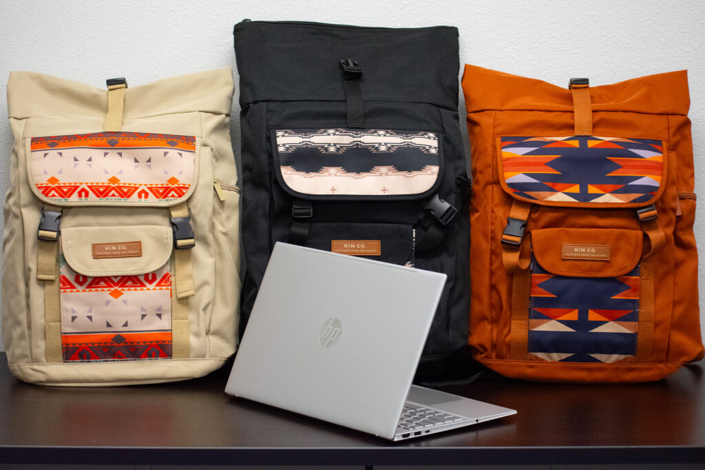 Three patterned backpacks by "KIN CO" and an HP laptop displayed on a table.