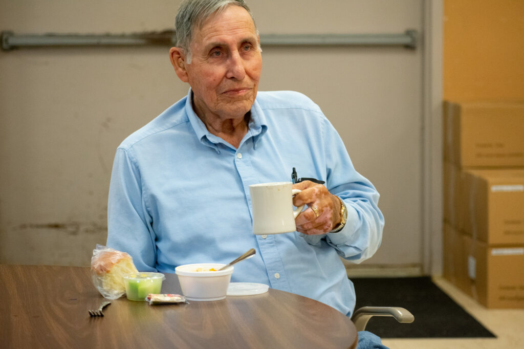 A man in a blue shirt holds a mug at a table with food items. Northern Plains Reservation Aid may be relevant.