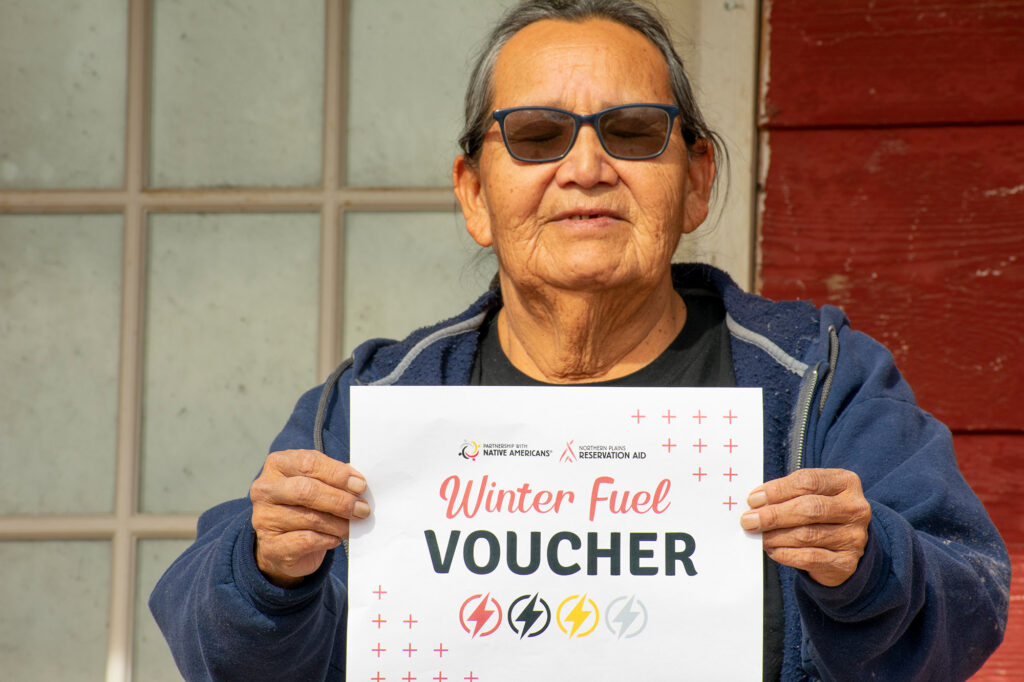 A person holding a "Winter Fuel Voucher" sign from Northern Plains Reservation Aid.