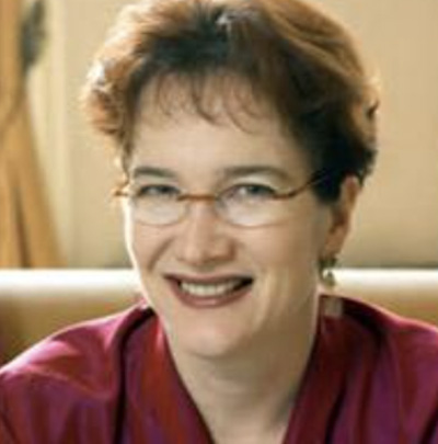 A person with glasses and short hair is smiling, wearing a red top.