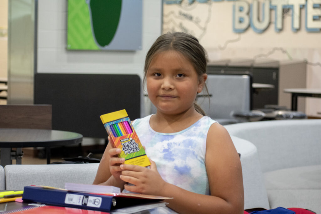 A young girl holding a pack of colored pencils, likely associated with school supplies.