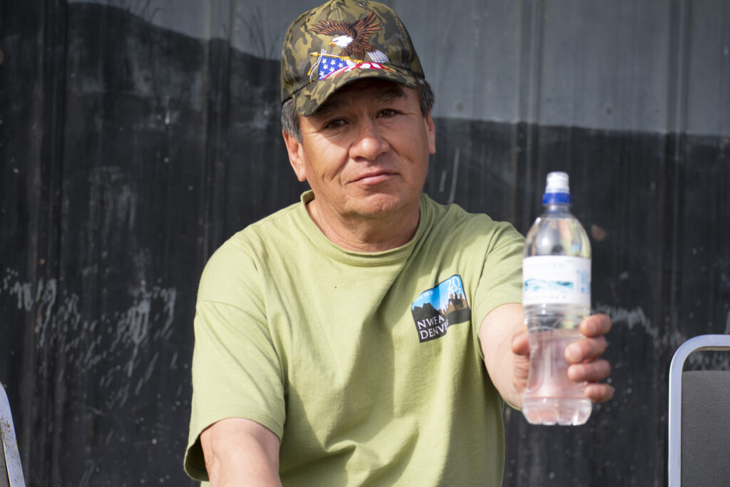 A person wearing a cap and green shirt is holding a water bottle.