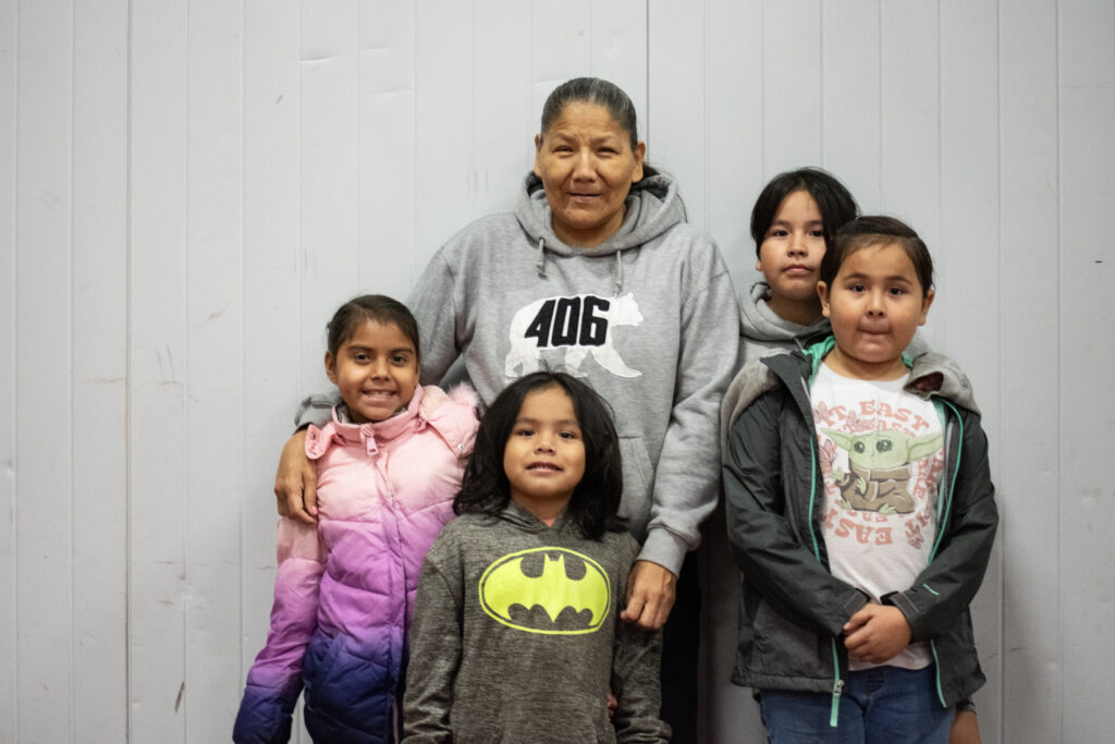 A group of five people, likely a family, stand together in front of a plain wall.