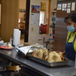 A person wearing a face mask and apron is preparing food in a kitchen.